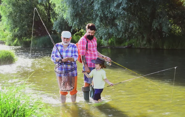 Morfars far och farfars sonson. Fiske blev en populär fritidsaktivitet. Glad farfar, far och sonson med fiskespön på flodbädd. — Stockfoto