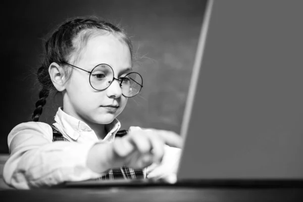 Leerling werkt aan laptop computer over schoolbord achtergrond. Kind in de buurt van schoolbord in de klas. Kind leert in de klas op de achtergrond van schoolbord. — Stockfoto