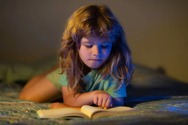 暗い家で本を読んでいる子供。小さな男の子のリビングルームに物語の本の中で写真を見て座っている。子供は小学校で宿題をしている。子供勉強. — ストック写真