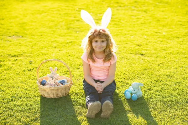 Barnpojke med påskägg och kaninöron utomhus. Söt unge som har en glad påsk i parken. Barn i kaninöron på påskäggsjakt i trädgården. — Stockfoto