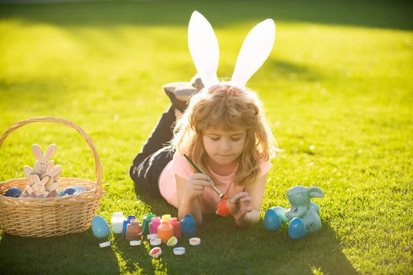 Paashaas kinderen. Kind jongen in konijn Pasen oren schilderen eieren. — Stockfoto