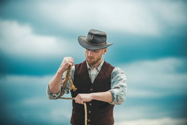 Guy cowboy. Owner of ranch. Farm worker and farming concept. Handsome man in cowboy hat and rustic style outfit. Cowboy with lasso rope on sky background. — Stock Photo, Image