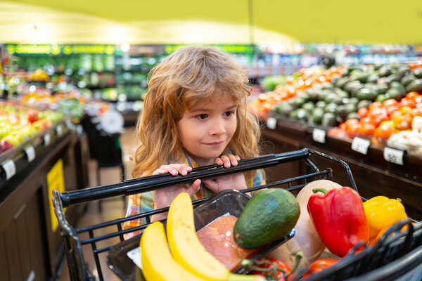 Здоровое питание для молодой семьи с детьми. Портрет улыбающегося малыша с корзиной со свежими овощами. Маленький ребенок выбирает свежие овощи в продовольственном магазине.