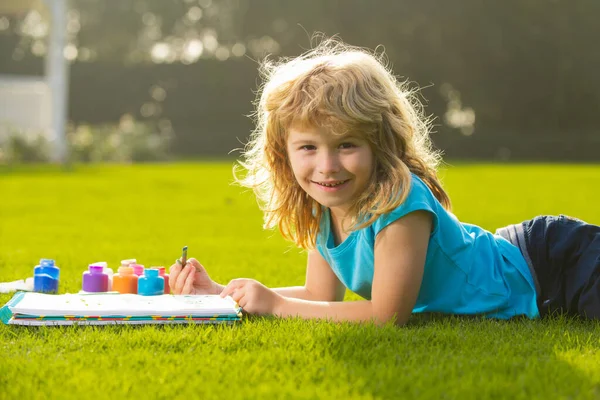Child drawing. Kid draws in park laying in grass having fun on nature background. Royalty Free Stock Photos