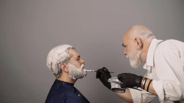 Профессиональный парикмахер, умирающий волосы бородатого человека в парикмахерской. Профессиональный парикмахер сушит волосы в студии. — стоковое видео