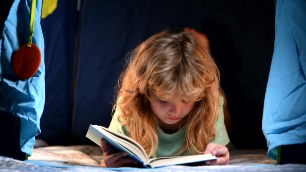 Niño leyendo un libro en la casa oscura. Infancia feliz, niño soñando leer cuentos para dormir, cuento de hadas o cuento de hadas. — Vídeo de stock
