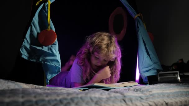 子供のテント読書本の子供の男の子。寝る前にベッドで本を読んでいる子供。子供は就寝時に本を読んでいます。少年読書就寝時の話おとぎ話. — ストック動画