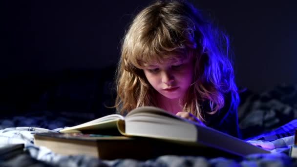 Lindo niño leyendo un libro de magia sobre fondo oscuro. Niño leyendo un libro en la noche a la hora de dormir. — Vídeo de stock
