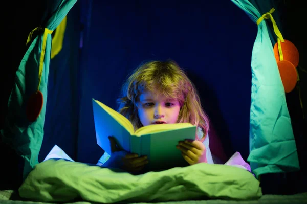 Çocuk kitap okuyor. Bilgiye doğru. Kitap okuyan çocuk karanlık gece odası arka planında hikaye okudu. Okumak için harika çocuk kitapları. Çocuk edebiyatı. — Stok fotoğraf