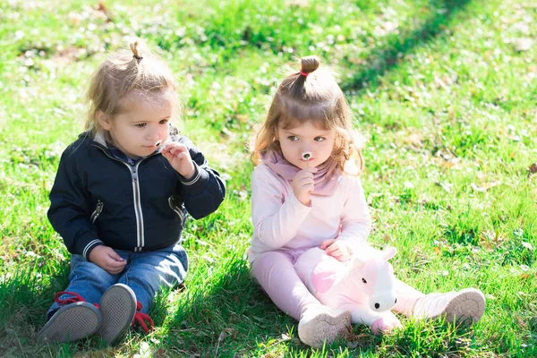 Söt pojke och flicka på vårfältet. Aktiviteter för barn utomhus. Familjesemester med barn. Glada barn som leker sittande på grönt gräs i vårparken. — Stockfoto