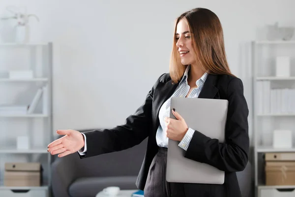 Porträt einer Geschäftsfrau mit Laptop, die am Arbeitsplatz im Büro Hand anlegt. Sekretär willkommen Handschlag, Grußwort Interview. Beziehung zum Geschäftspartner. — Stockfoto