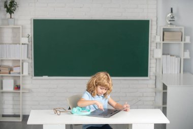 Okul çocuğu sınıfta dijital bilgisayar kullanıyor. İlkokul öğrenim programının komik öğrencisinin portresi.