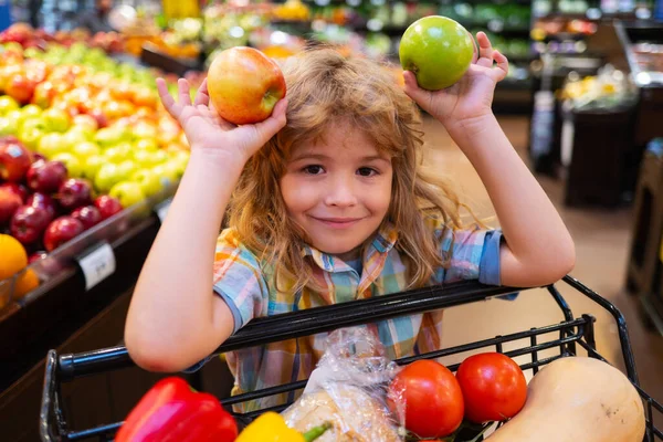 Bambino che sceglie una mela in un negozio. Divertente bambino sorridere e tenere la mela. Un ragazzo che fa shopping al supermercato. Bambino che sceglie verdure fresche in un negozio di alimentari. — Foto Stock