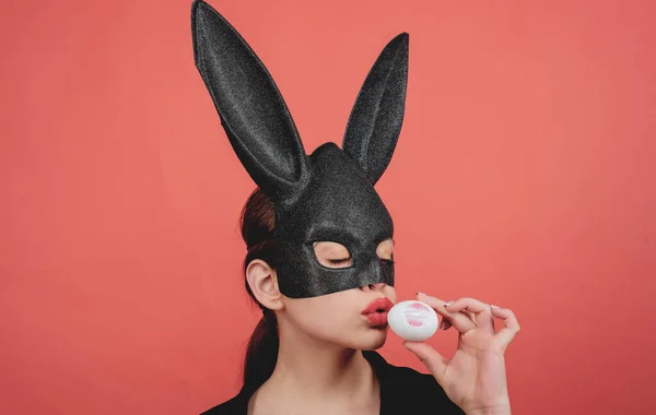 Máscara de conejo mujer. Beso de boca femenina. Lápiz labial beso huella. Huella de labio rojo en huevo de Pascua sobre fondo rojo. Joven pascua, mujer en orejas de conejo . — Foto de Stock