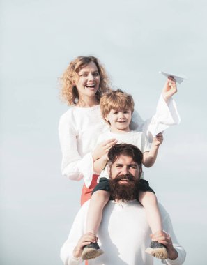 Baba anne ve oğlu dışarıda oynuyorlar. Yaz istihkakı. Sevimli küçük çocuk kağıt uçak tutuyor. Mutlu bir aile. Ebeveynler ve çocuk. Mutlu aile ve küçük oğlu mavi yaz gökyüzünde oynuyor.