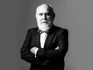 Kolları çapraz yaşlı adam. Gri saçlı, kıdemli, şık takım elbiseli ve kravatlı, kendine güvenen bir iş adamı..