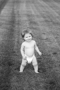 Yaz akşamında çimlerin üzerinde mutlu bir bebek. Dışarıda gülümseyen bir çocuk. Mutlu çocukluk ve çocuk sağlığı hizmetleri.