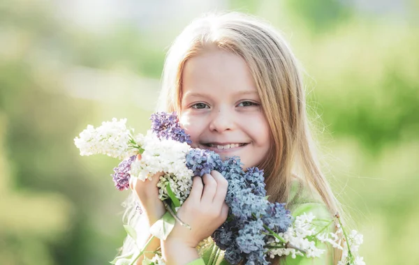 Cheerful young little lady in the garden with long fair hair being excited to get a bouquet of lilac on womens day. — Stock Photo, Image