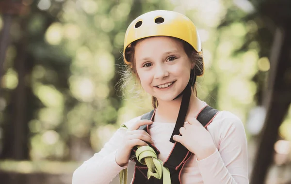 Portret van een mooi kind op een touw park tussen de bomen. Gelukkig klein meisje klimmen een boom. Helm-veiligheidsuitrusting voor klein meisje spelen. Speeltuin. Veilig klimmen extreme sport met helm. — Stockfoto