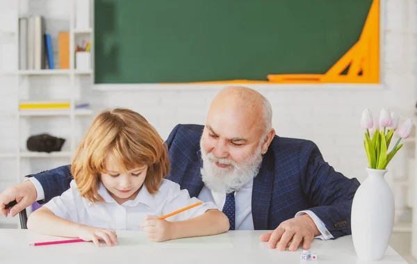Végzős tanár vagy nagyapa és iskolás fiú a suliban. Általános tanuló olvasás és írás tanárral az osztályteremben. — Stock Fotó