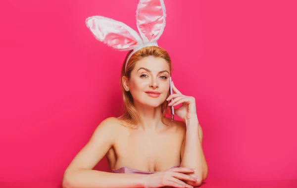 Femme de Pâques avec des oreilles de lapin parlant au téléphone isolé sur une bannière rose, espace de copie. — Photo