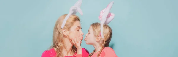 Moeder en dochter met Pasen. Familie viert Pasen. Meisjes met konijnenoren kussen, geïsoleerd op blauw. Pasen banner met kopieerruimte. — Stockfoto