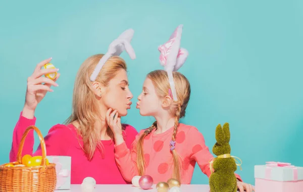 Szczęśliwego Wielkanocy. Matka i jej córka malują wielkanocne jajka i całują się. Szczęśliwa rodzina przygotowuje się do Wielkanocy. słodkie małe dziecko dziewczyna noszenie królicze uszy na Wielkanoc dzień odizolowany na niebieski. — Zdjęcie stockowe