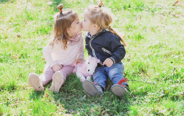 Miúdos giros adoram. Menina beijando menino pequeno ao ar livre no parque. Crianças em belo campo verde primavera. — Fotografia de Stock