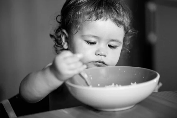 Happy baby eating himself with a spoon. Child nutrition concept. — Stock Photo, Image