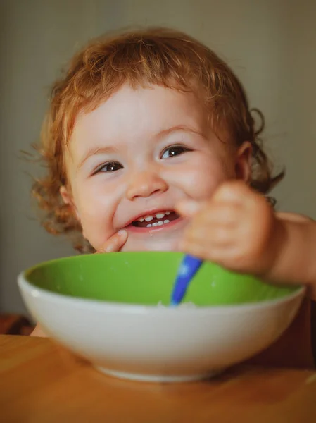Baby houdt een lepel in zijn mond. Gelukkig kind eet zichzelf op met een lepel. Lancering van het eten van voedsel door kinderen. — Stockfoto