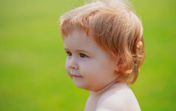 Porträtt av en liten pojke som leker utomhus i gräset. Baby ansikte på nära håll. Lustigt litet barnporträtt. Blond unge, känslomässigt ansikte. — Stockfoto