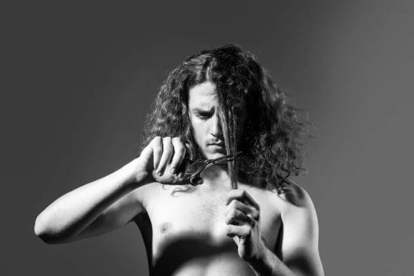 Jeune homme, portrait d'un gars avec des ciseaux de coiffeur pour salon de coiffure, couper de longs cheveux bouclés. Beau mâle avec coiffure moderne sur noir. — Photo