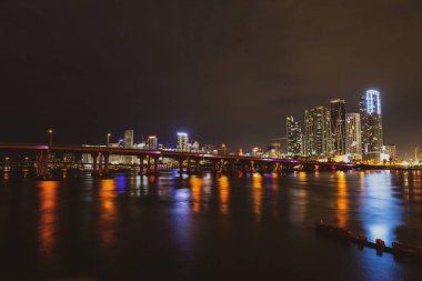 Şehir merkezinde Miami gecesi. Miami Florida, gün batımı manzarası. Biscayne Körfezi 'nde renkli iş yerleri, konut binaları ve köprü..
