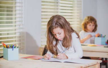 Okul sınıfında masada oturan sevimli bir kızın portresi. Öğrenci çizimleri, anaokulu çocuk çalışmaları. Çocuk eğitimi, evde eğitim kavramı.