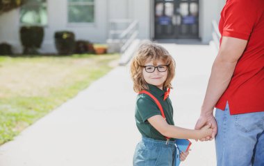 Baba oğul okul parkında yürüyorlar. Öğretmenlerin elini tutan mutlu inek öğrenci portresi..