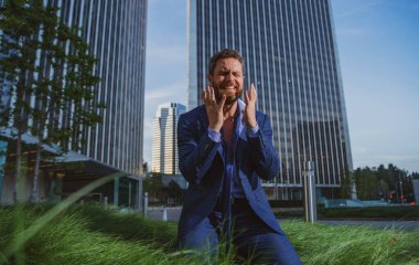 Depresyonda ağlayan bir iş adamı çimenlerde oturup duygusal acı, üzüntü, şok olmuş ve öfkeli görünüyor..