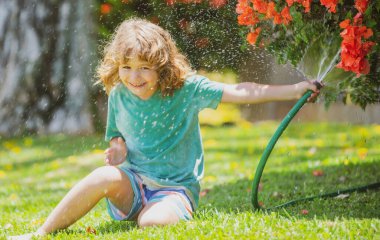 Arka bahçede bahçe hortumuyla oynayan komik çocuk. Çocuk su püskürterek eğleniyor. Çocuklar için yaz açık hava aktivitesi.