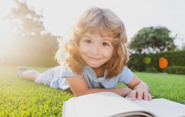 Çimlerin üzerinde kitap okuyan sevimli çocuk. Çocuk yaz parkında kitap okuyor..