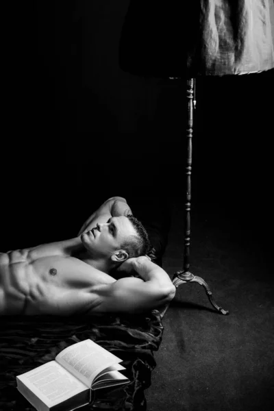 Красивый молодой человек без рубашки читает книгу в постели. Умный и умный гей. — стоковое фото