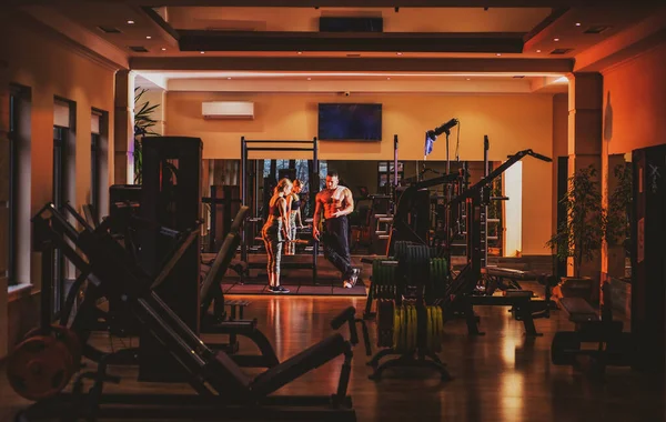Sporty couple in gym. Personal trainer helping woman doing exercise. — Zdjęcie stockowe