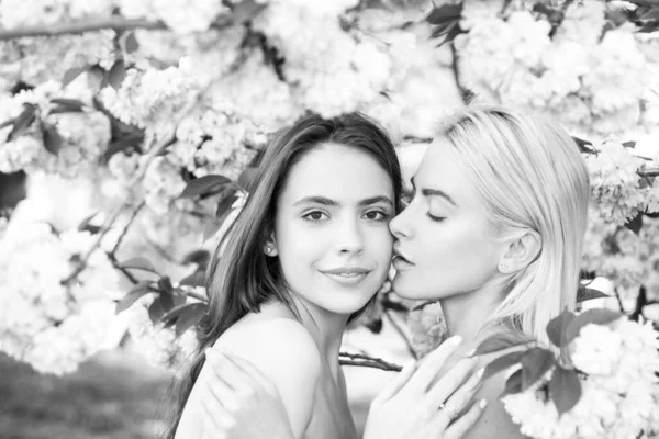 Porträtt av två vackra vårflickor. Två unga kvinnor som kopplar av i Sakura blommor. Lesbiska par kysser varandra. Känslig beröring och kyss. Flickvänner. — Stockfoto