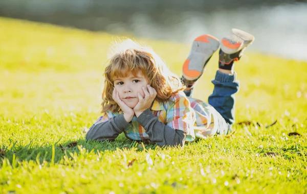 子供の屋外。公園の子供だ。春の少年草の上に横たわる。夏の散歩。子供の適応. — ストック写真
