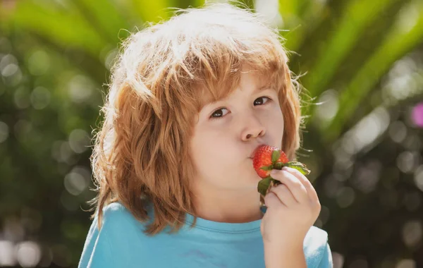 Niño comiendo fresa en la naturaleza. Niño disfruta de una deliciosa baya sobre fondo verde de verano. Cerca de los niños cara feliz. — Foto de Stock