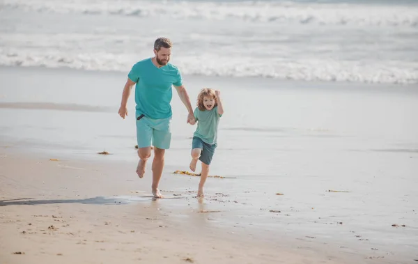 Πατέρας και γιος τρέχουν στην καλοκαιρινή παραλία. Ο μπαμπάς και το παιδί διασκεδάζουν έξω.. — Φωτογραφία Αρχείου