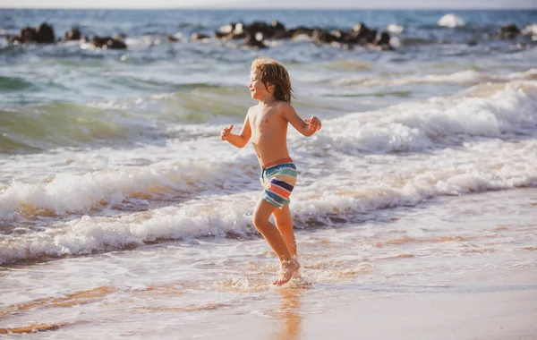 Mały chłopiec biegający po plaży, rozpryskujący wodę w błękitnym morzu. Dzieciak spacerujący po letniej plaży. — Zdjęcie stockowe