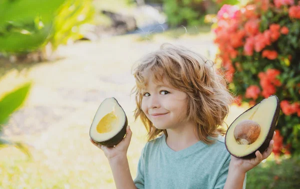 Close-up gezicht van kind met een halve avocado in haar handat tropische tuin. Gezonde kinderen avocado food concept. — Stockfoto