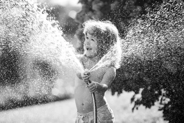 Niño jugando en el jardín, vierte de la manguera, hace una lluvia. Concepto de infancia feliz. — Foto de Stock