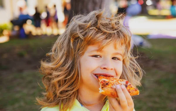 Pizzadan bir ısırık alan bir çocuk. Çocuk bir dilim pepperoni pizza yiyor. Komik çocuk suratı. — Stok fotoğraf