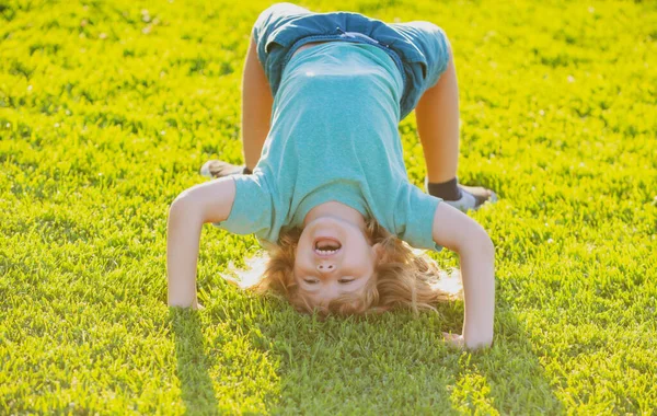 Happy kid garçon fille debout à l'envers sur sa tête sur l'herbe dans la journée d'été. — Photo