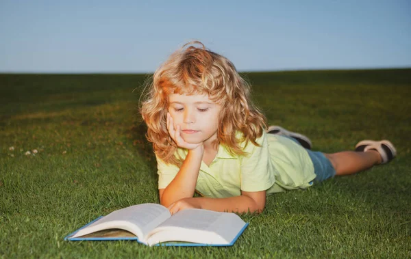 Skolpojke med en bok som vilar utomhus. Barnpojke med en bok i trädgården. Ungen läser en bok som leker utomhus på sommardagen.. — Stockfoto